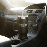 Black Stand Firm tumbler in car cup holder with morning sunlight